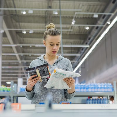 A woman reading nutrition labels on frozen food items in a supermarket