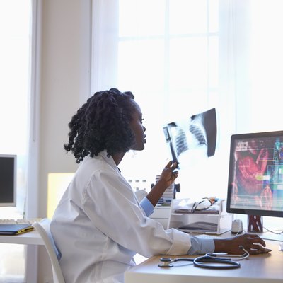 Black doctor examining chest x-ray and using computer