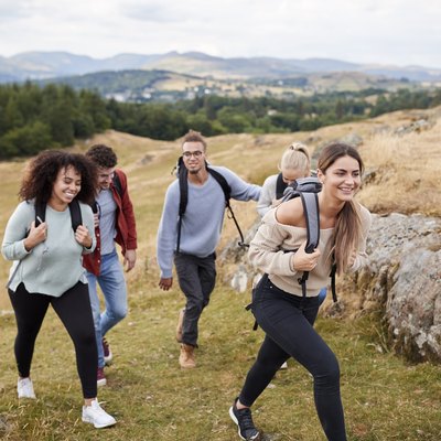 Multi ethnic group of five young adult friends hiking across a field uphill towards the summit, close up