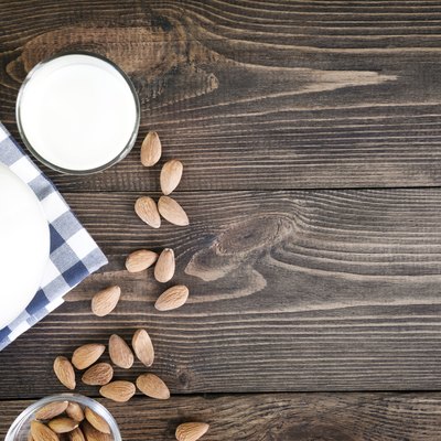 Fresh almond milk in glass and pitcher on dark wooden table. Rustic style.