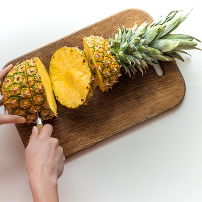 person cutting fresh pineapple on wooden board