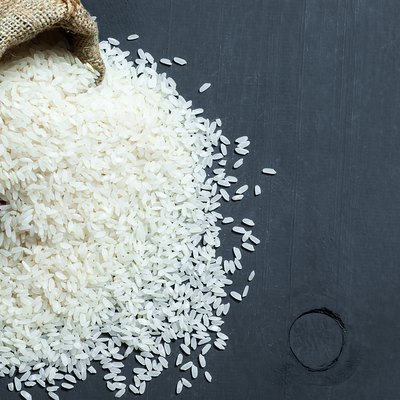 turkish raw white rice grains in burlap sack on black wooden background