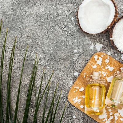 top view of coconut oil in bottles on wooden board on grey textured background with copy space and palm leaf
