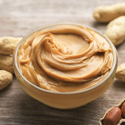 Glass bowl with peanut butter on wooden background