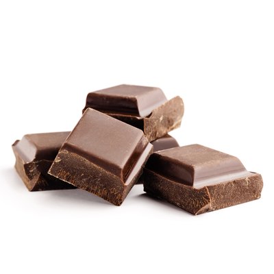 Pieces of bitter, dark chocolate bar, cubes on heap, isolated on white background, close-up view