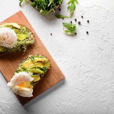 Tasty toasts with avocado and eggs Benedict on wooden board