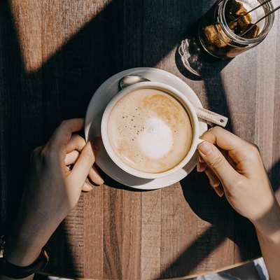 Top view of woman sitting by the window in coffee shop enjoying the warmth of sunlight and drinking coffee
