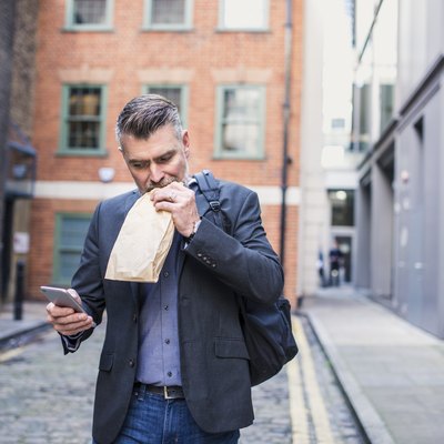 Businessman eating a sandwich and using smart phone