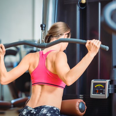 Strong fit woman exercising lat pushdown for back muscles in a modern fitness club