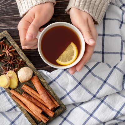 Female hands holding cup of tea with lemon on wooden table