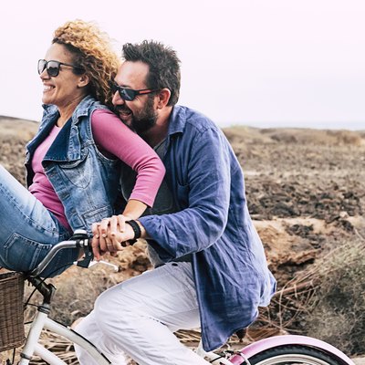 happy adult caucasian, couple having fun with bicycle in outdoor leisure activity. concept of active playful people with bike during vacation - everyday joy lifestyle without age limitation - man carry woman and both have fun and laugh a lot with wind in