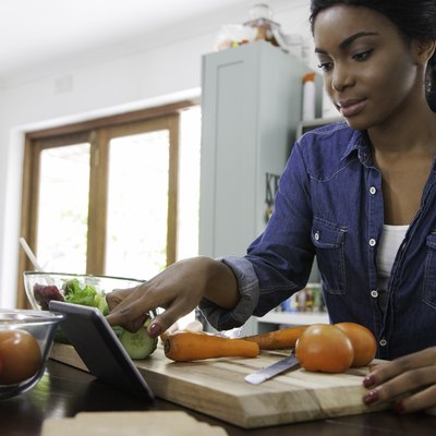 An African-American woman using her tablet to track Weight Watchers points as she cooks dinner