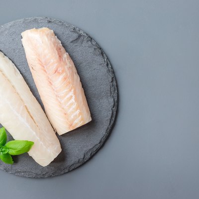 Fresh raw cod fillet with basil on stone plate, horizontal, copy space, top view