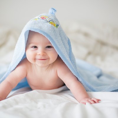 Cute little baby boy, relaxing in bed after bath, smiling happily