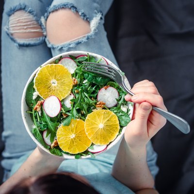 Woman in jeans at bed, holding vegan salad bowl