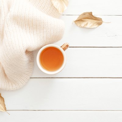 Cozy home desk table with knitted plaid, tea cup, fall leaves on wooden white background. Top view, flat lay, copy space. Autumn composition. Nordic hygge style concept.