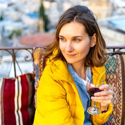 Woman is enjoying the glass of wine on the balcony at sunset