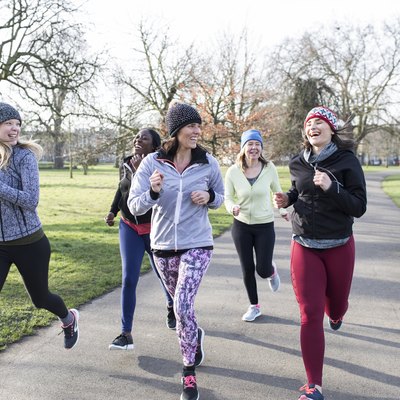 Smiling female runners running in sunny park