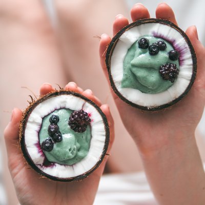 Two coconut half spirulina smoothie in woman hands
