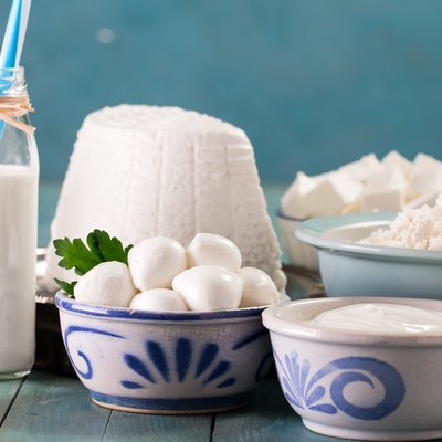 tasty healthy fermented dairy products on a table on a blue background: sour cream, cottage cheese, mozzarella cheese, butter,ricotta and milk in a bottle