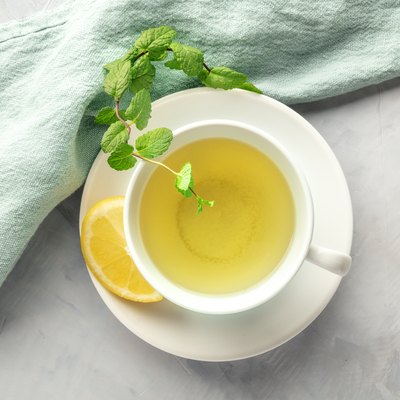 A cup of green tea with lemon and mint leaves.