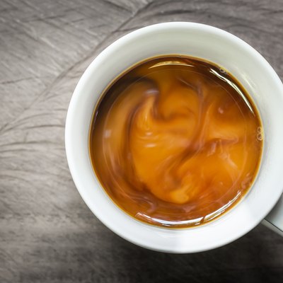Cup of coffee with flowing milk on wooden background, overhead shot.