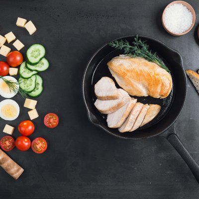 Fried chicken breast on a cast iron frying pan and fresh sliced vegetables