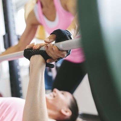 Two women doing barbell bench presses in a power rack