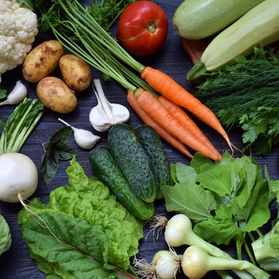 Composition on a dark background of organic vegetarian products: green leafy vegetables, carrots, zucchini, potatoes, onions, garlic, tomatoes. Top view
