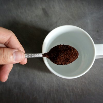Hand Holding Spoon Of Coffee Powder Over Cup