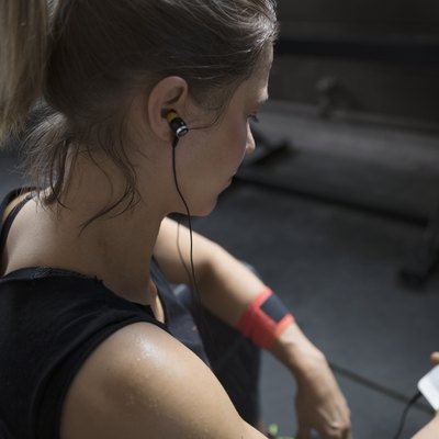 Woman weightlifting, resting and listening to music with headphones and mp3 player at gym