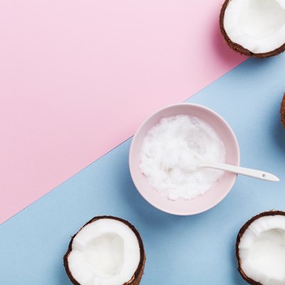 Coconut oil with fresh coconuts fruit on minimal pastel background top view. Natural and organic beauty cosmetic.