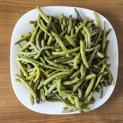 White plate of green beans boiled on a wooden table. Spain
