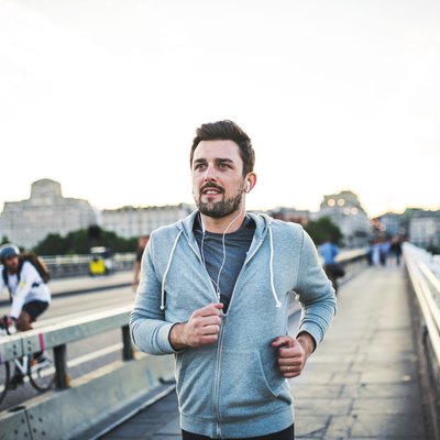 Young sporty man with earphones running on the bridge outside in a city.