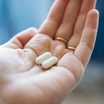 Close-up view of a hand holding two white pills in the palm above a blurry background, painkiller
