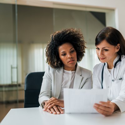 Portrait of a beautiful female doctor and patient looking at cholesterol test results.