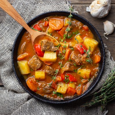 Goulash, beef stew or bogrash soup with meat, vegetables and spices in cast iron pan on wooden table.