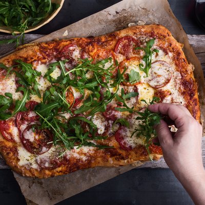 Preparing gourmet pizza, close-up of hand topping pizza with arugula