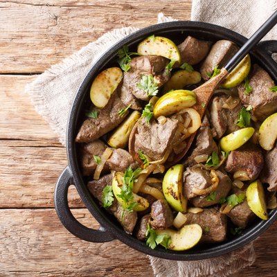 German food fried beef liver with green apples and onions close-up in a pan. Horizontal top view