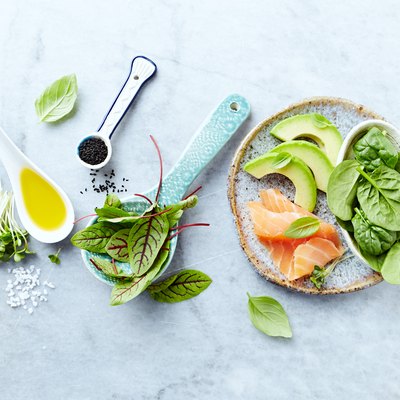 Ingredients for a healthy salad on gray stone background. Smoked salmon, avocado, spinach, sorrel, radis sprouts, black cumin. Flat lay. Healthy diet. Symbolic image.