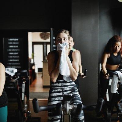 Woman wiping sweat from face with towel during indoor cycling class in fitness studio
