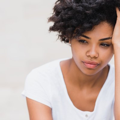 Beautiful young black woman with sad, pensive, reflective look, against white wall background. Portait of worry dark skinned female in white t-shirt
