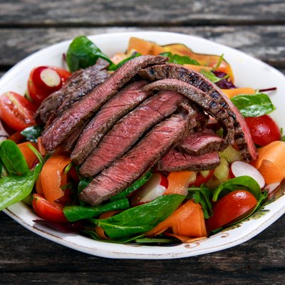 Slices of medium steak over a salad with mixed vegetables