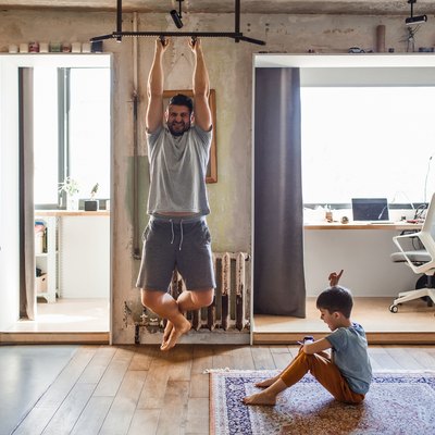 Dad doing pull-ups for the CrossFit Murph workout while his son plays nearby