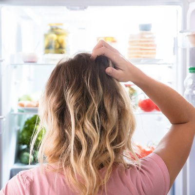 Confused woman with no appetite looking into refrigerator at home