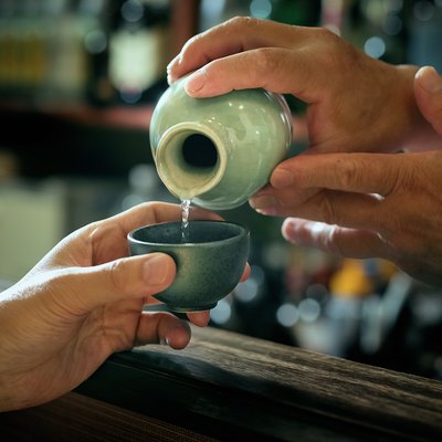 Close-up of bartender hand pouring Sake to glass which hands of adult man.