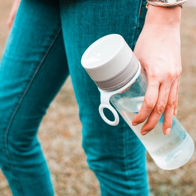 A young woman is holding a reusable water bottle container outdoors