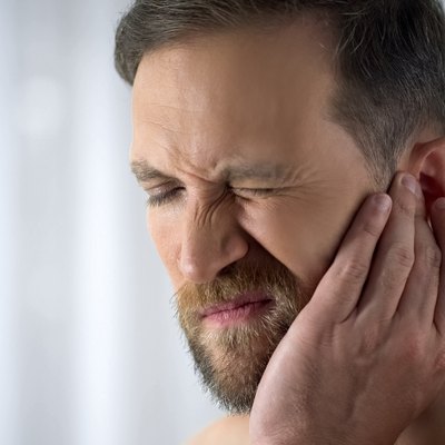 Man holding his aching ear, suffering from otitis, sudden hearing loss, close up