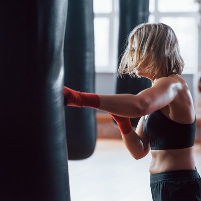 Full kickback. Female boxer is punching the bag. Blonde have exercise in the gym