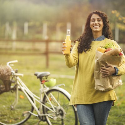 Woman drinking juice and holding shopping bag near her bicycle